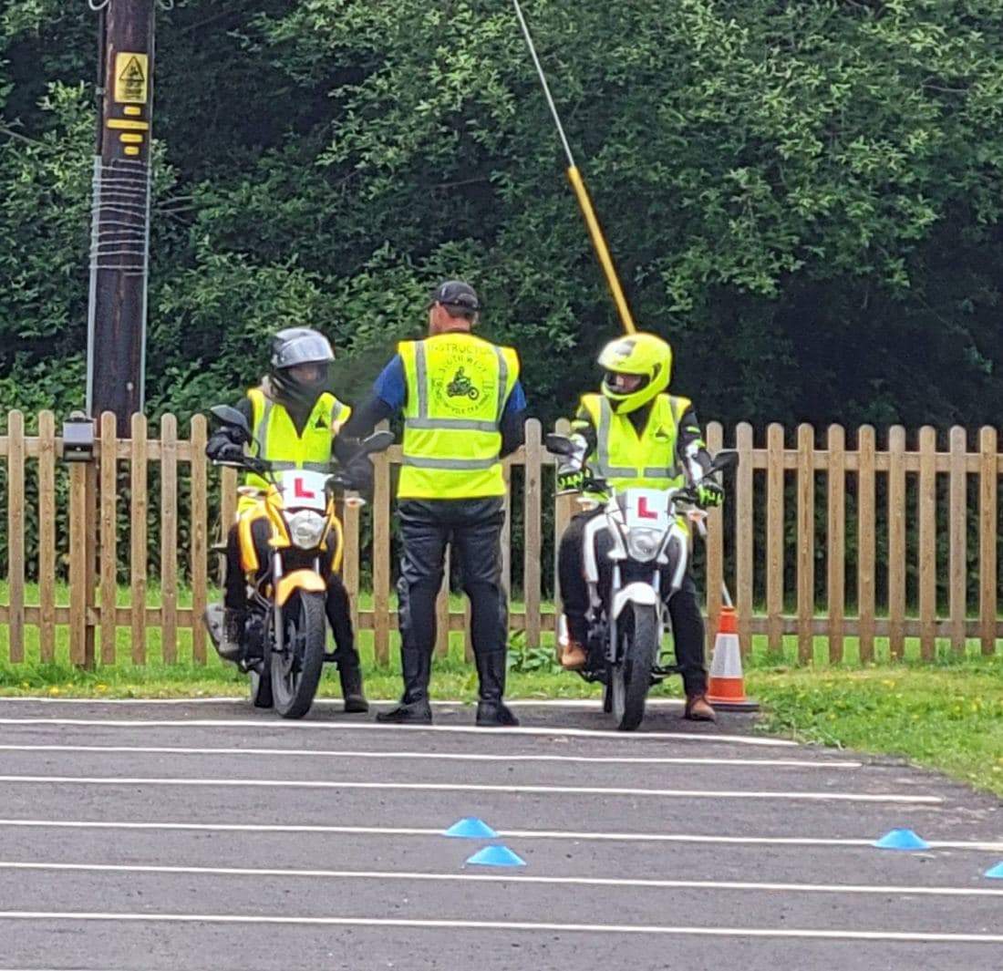 An instructor in hi-vis with two learner riders on L-plated training bikes on the manoeuvring pad at North Tawton An instructor in hi-vis with two learner riders on L-plated training bikes on the manoeuvring pad at North Tawton