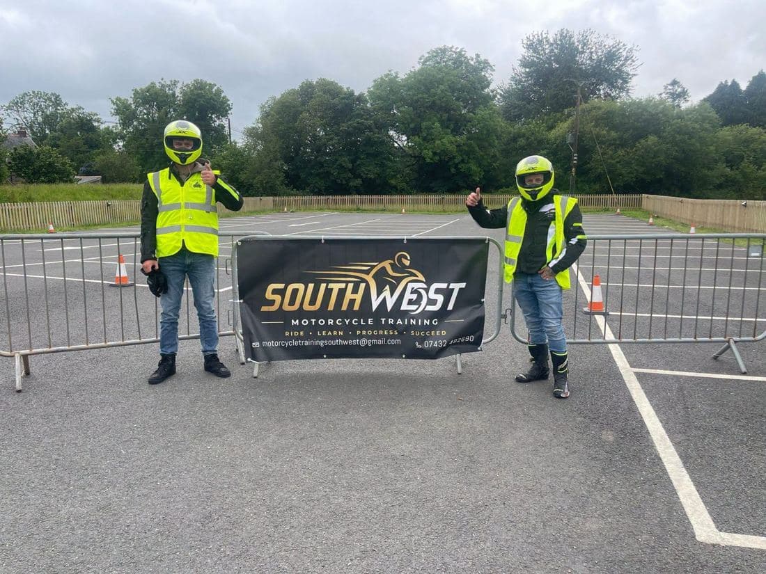 Two riders in helmets and hi-vis giving a thumbs up either side of the South West Motorcycle Training banner Two riders in helmets and hi-vis giving a thumbs up either side of the South West Motorcycle Training banner